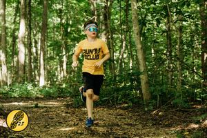 Trail runner wearing yellow t-shirt and blue cap runs through a sunlit forest on dirt path during summer.