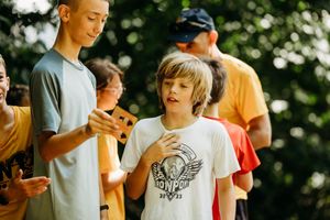 Youth in casual summer attire gather outdoors looking at mobile devices on a sunny day.