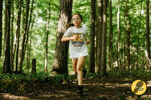Two people walk their mountain bikes through a lush green forest trail on a sunny summer day.