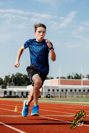 Runner in blue camo shirt and black shorts sprinting on red track during training session.
