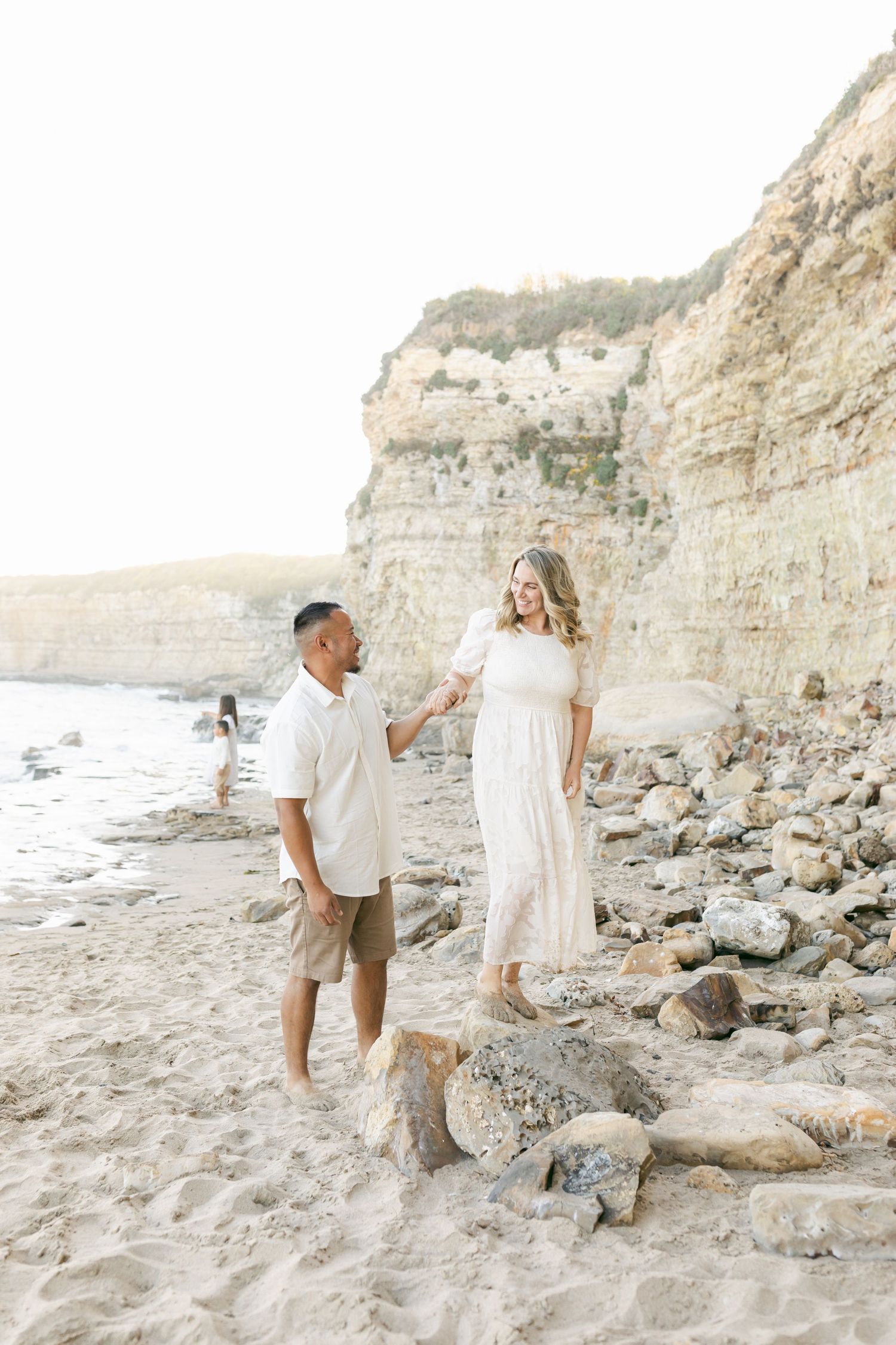 A couple enjoying a romantic beach photoshoot along scenic rocky cliffs during sunset captured by Chelsee Rawe Photography.