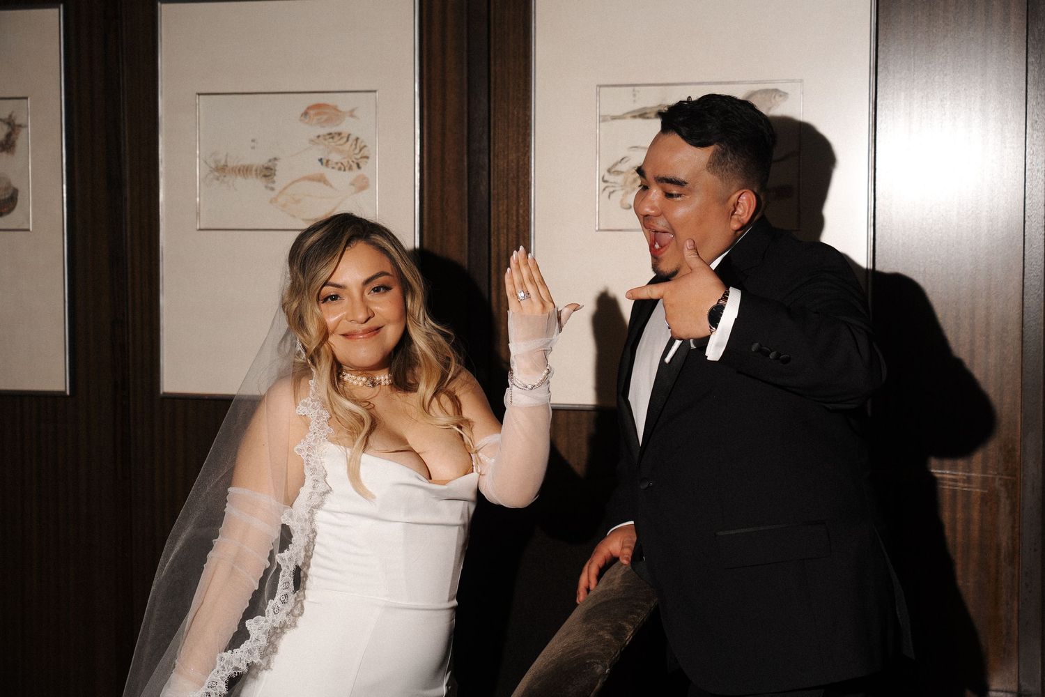Two people share a celebratory high five moment at a wedding reception, with dark wood paneling in the background.