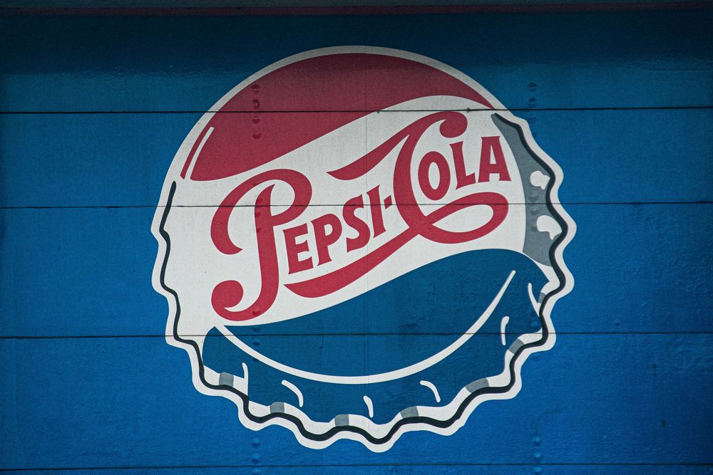 Vintage Pepsi-Cola bottle cap logo painted on blue wooden wall.