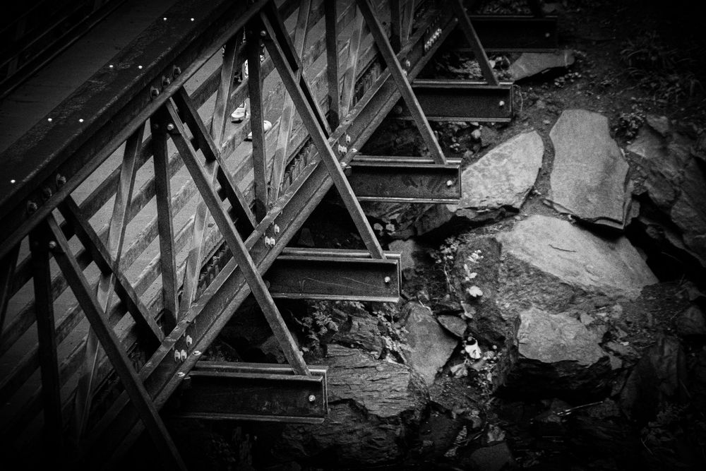 Black and white photo of rustic metal bridge support structure and rocks.