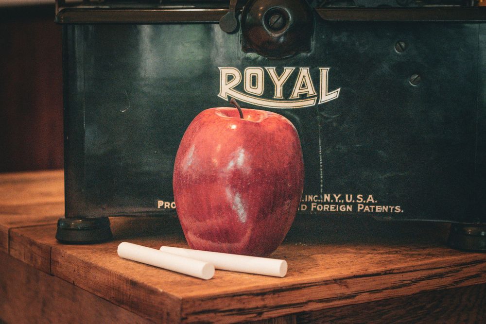 Red apple resting against vintage Royal typewriter on wooden surface.