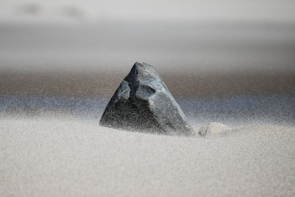 Minimalist composition of rocks emerging from smooth sand in monochromatic tones.