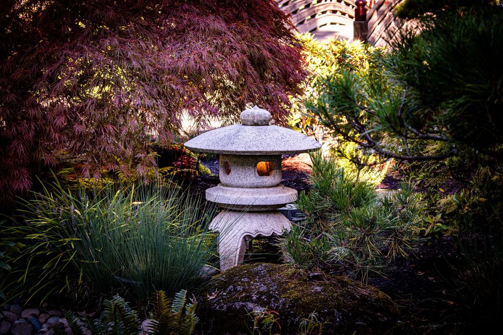 Stone pagoda lantern sits among colorful Japanese garden foliage at dusk.