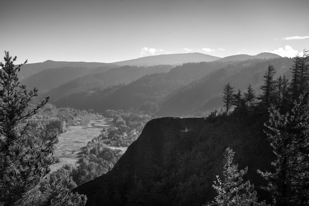 Black and white mountain landscape with deep valley and forested slopes.