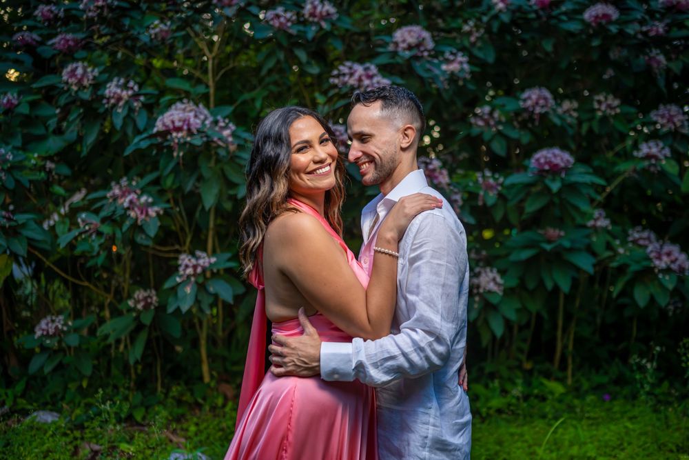 A romantic couple embraces among vibrant pink flowers in a lush garden setting during a photo session.