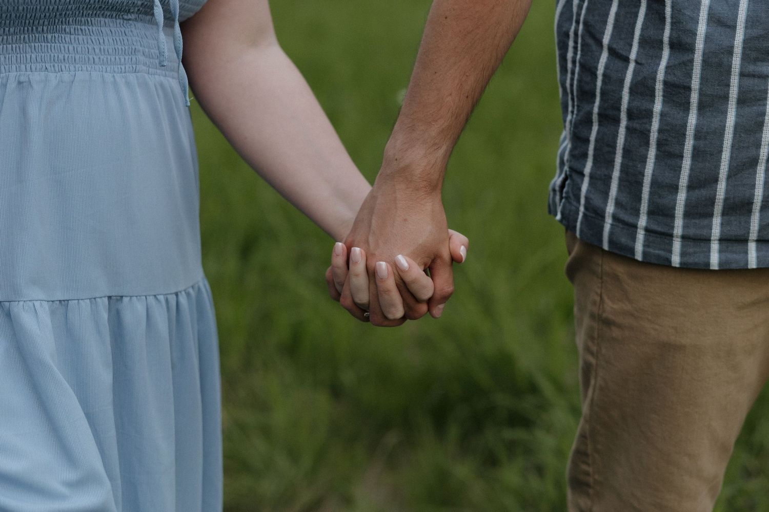 Close-up shot showing holding hands of people outdoors in casual clothing with green grass in background.