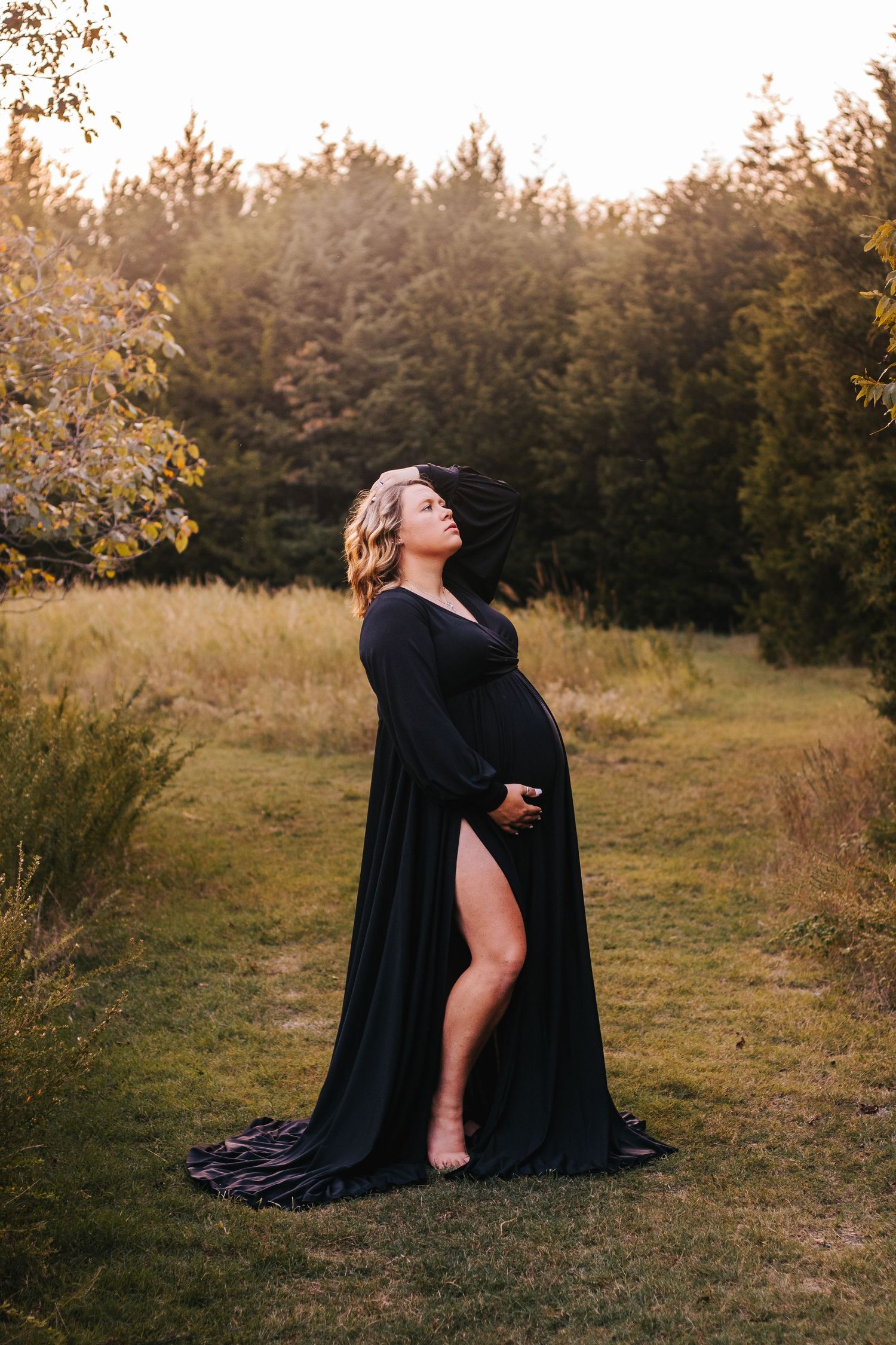 Artistic outdoor portrait session at sunset with flowing black cape in natural field setting.