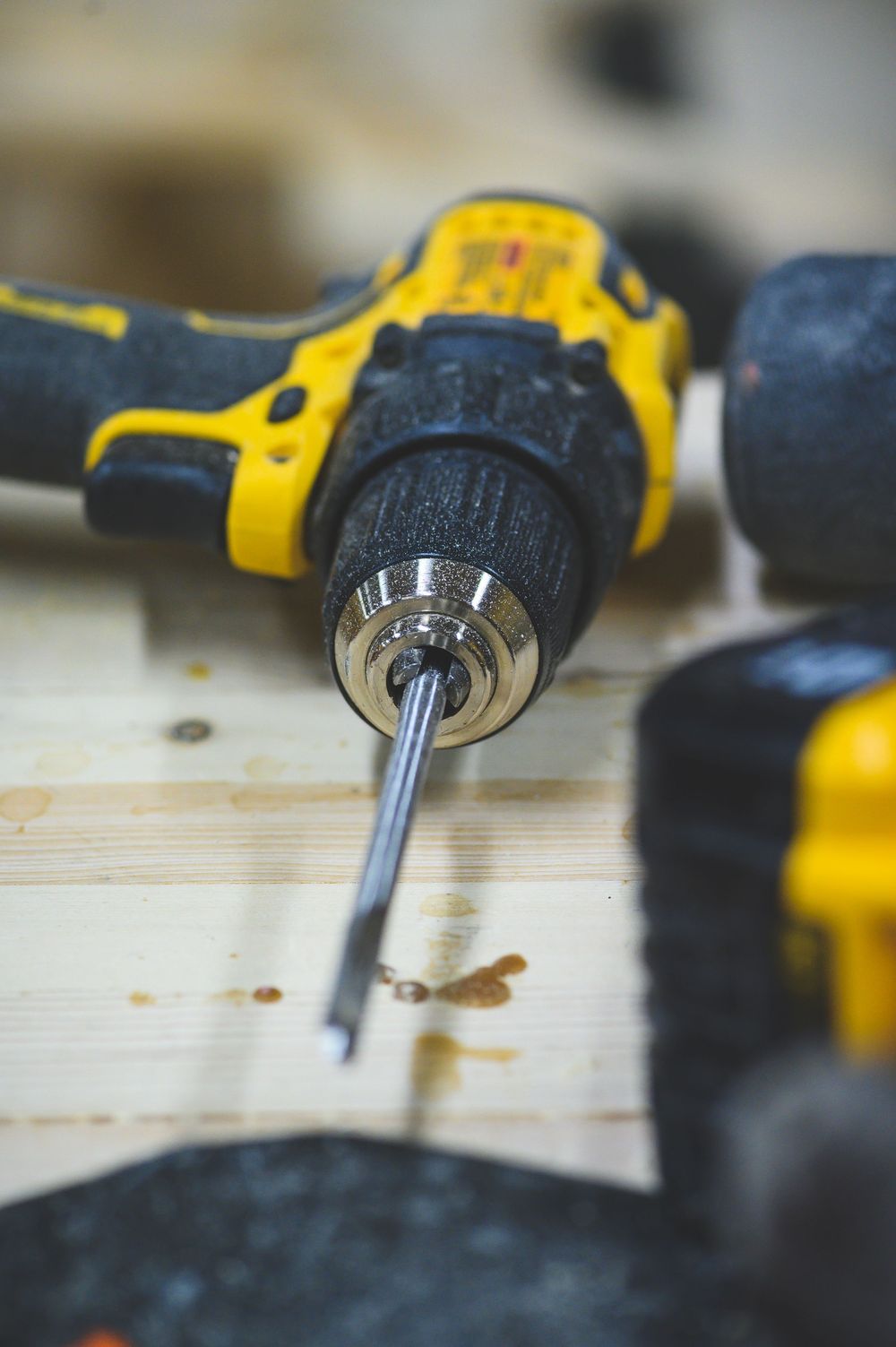 Close up view of yellow power drill driving screw into wood with blurred background.