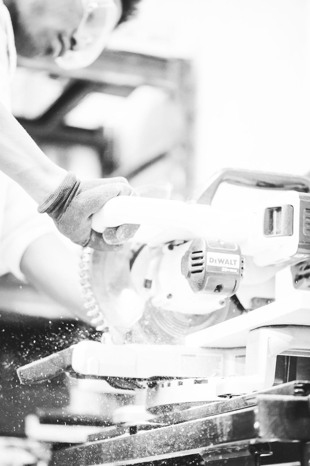 Close-up black and white shot of someone using a power sander on a woodworking project with sawdust flying.