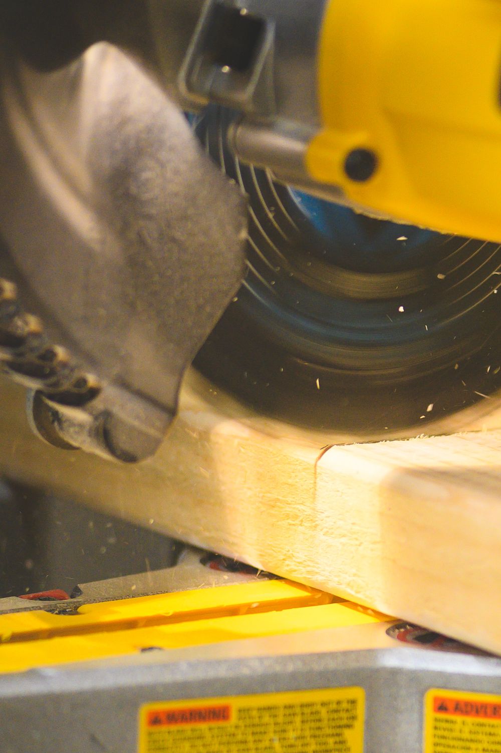 Close-up view of circular saw blade cutting through wooden surface in workshop with yellow safety guard visible.