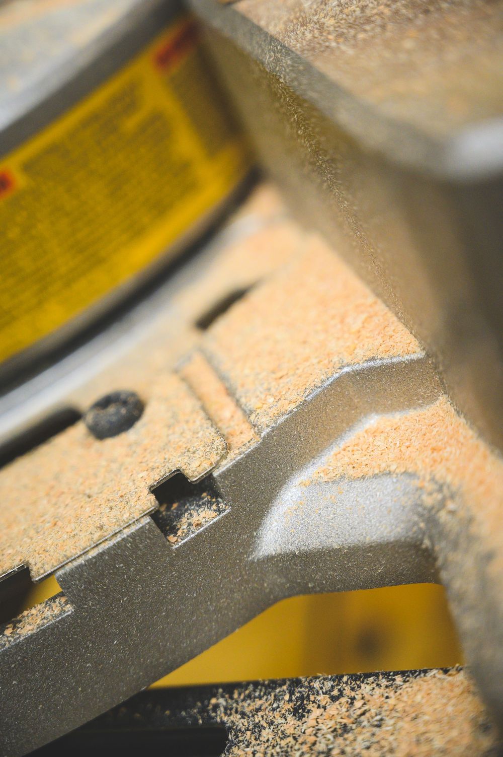 Close-up macro shot of a power tool blade showing sawdust and partial view of yellow warning label.