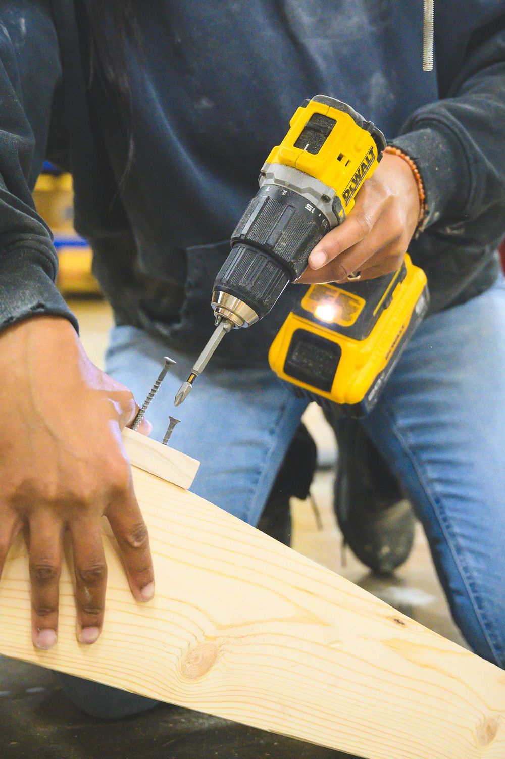 Someone using a yellow DeWalt cordless drill to make holes in a piece of light-colored wood.