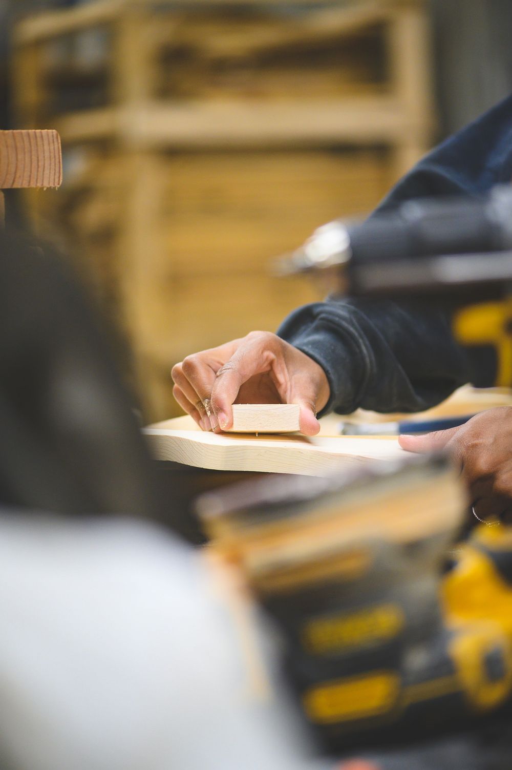 Close-up of hands sanding wood with sandpaper in a woodworking workshop with tools in background.