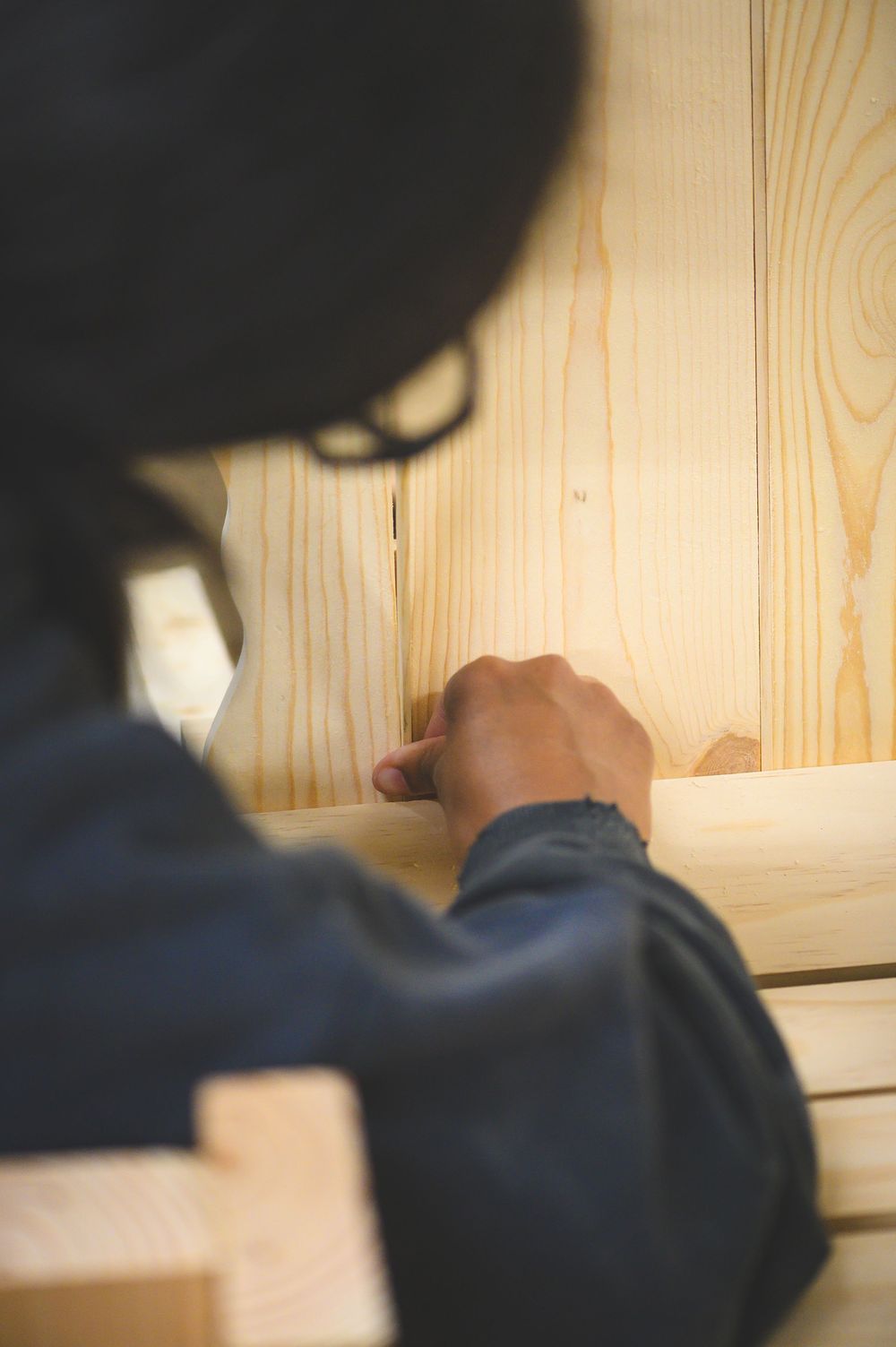 Close-up view of hands working with light wooden planks against a natural pine wood chair.