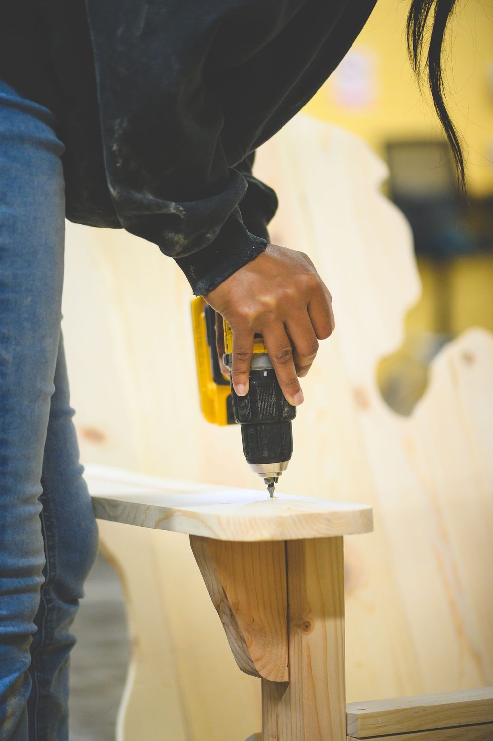 Person using a power drill on wooden furniture during a DIY home improvement project.