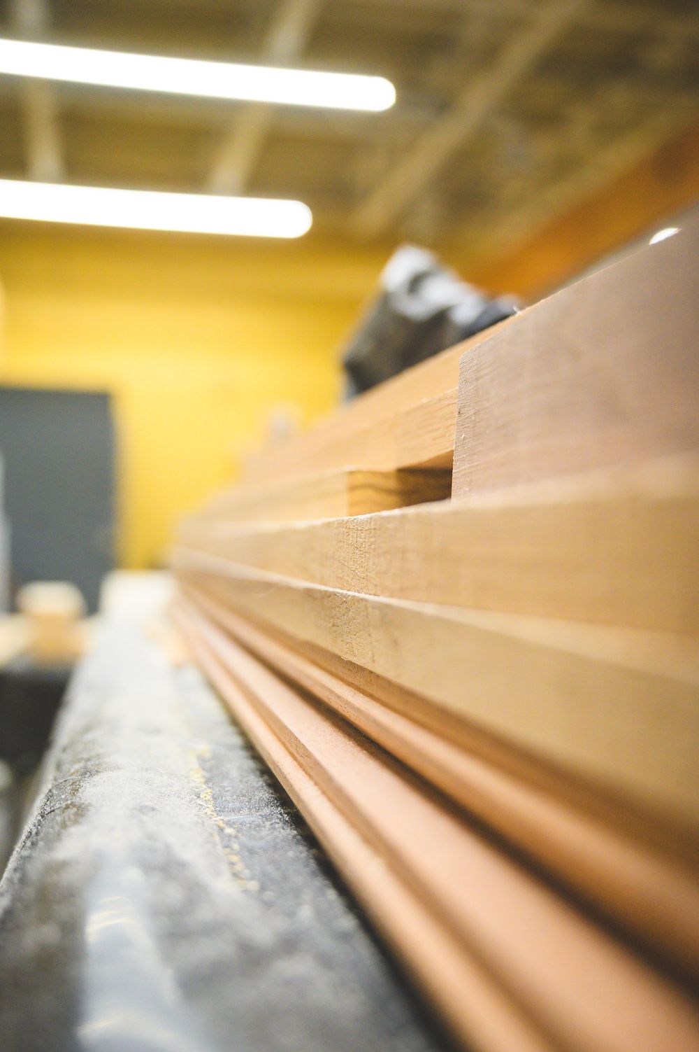 Close-up shot of wooden trim molding pieces stacked on a workbench in a carpentry workshop with warm lighting.