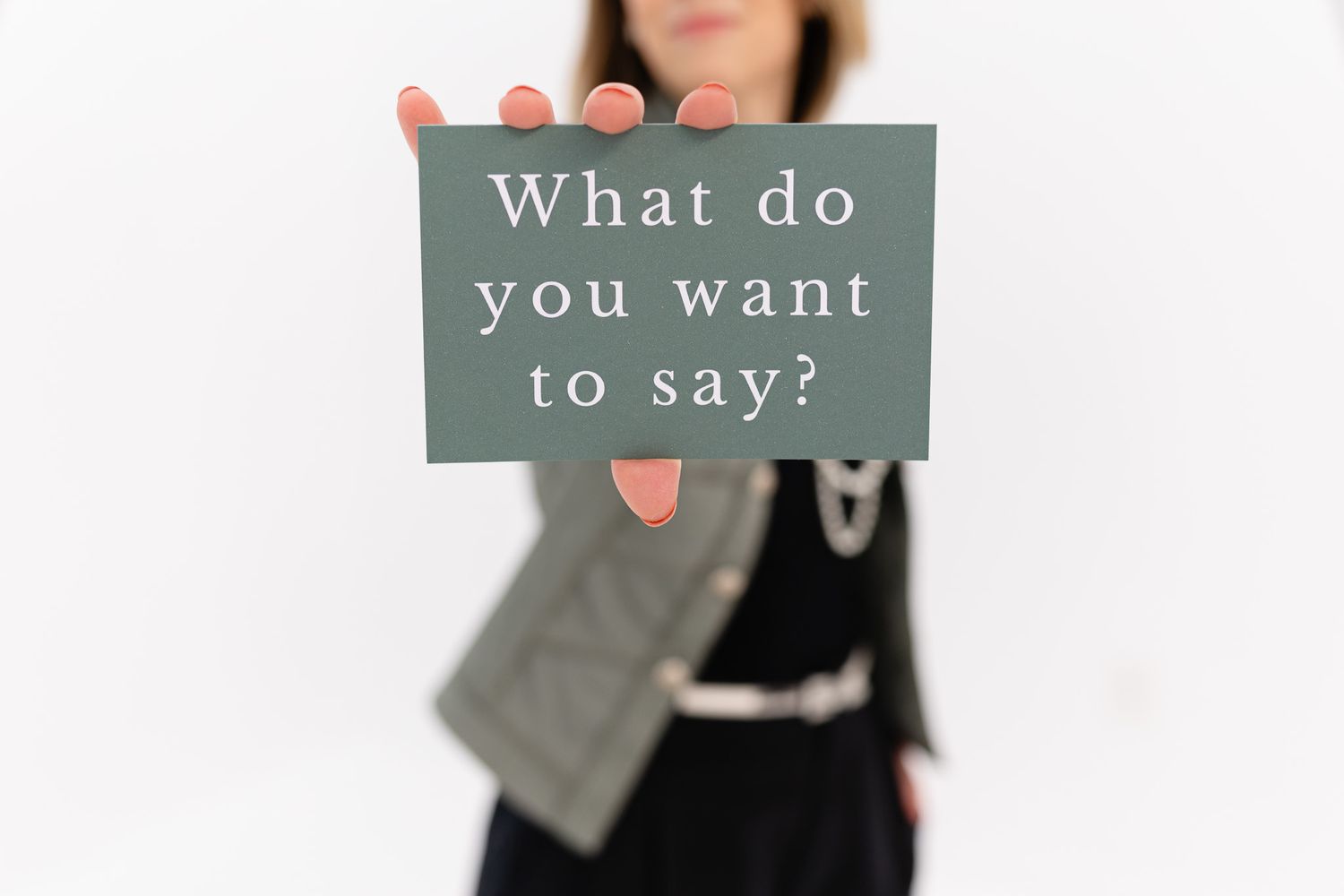 Person holds up gray cards with text reading 'What do you want to say' against light background.
