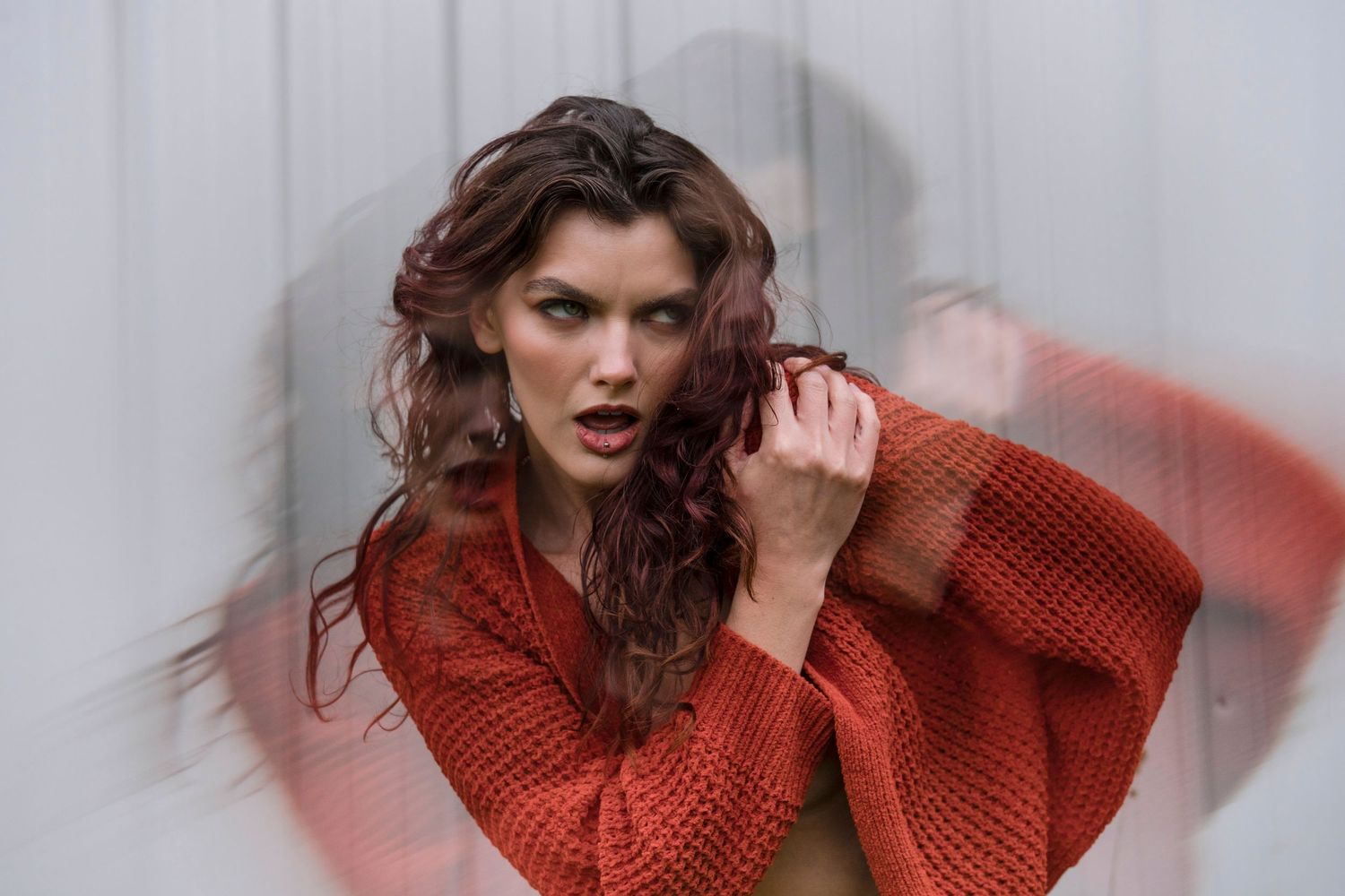 Fashion portrait in a red knit sweater with dramatic volume sleeves against a light background.