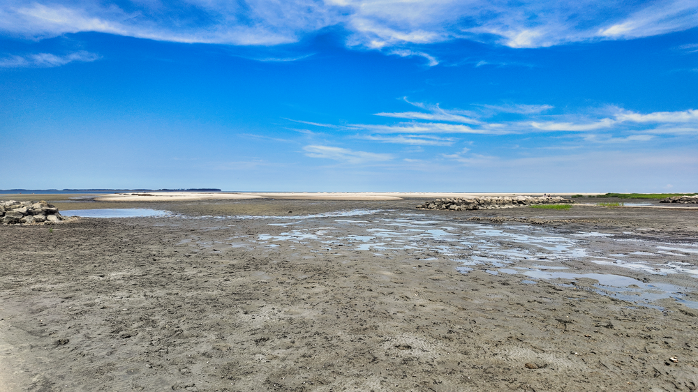 Salt flats extend across a vast desert landscape under bright blue skies with scattered white clouds.
