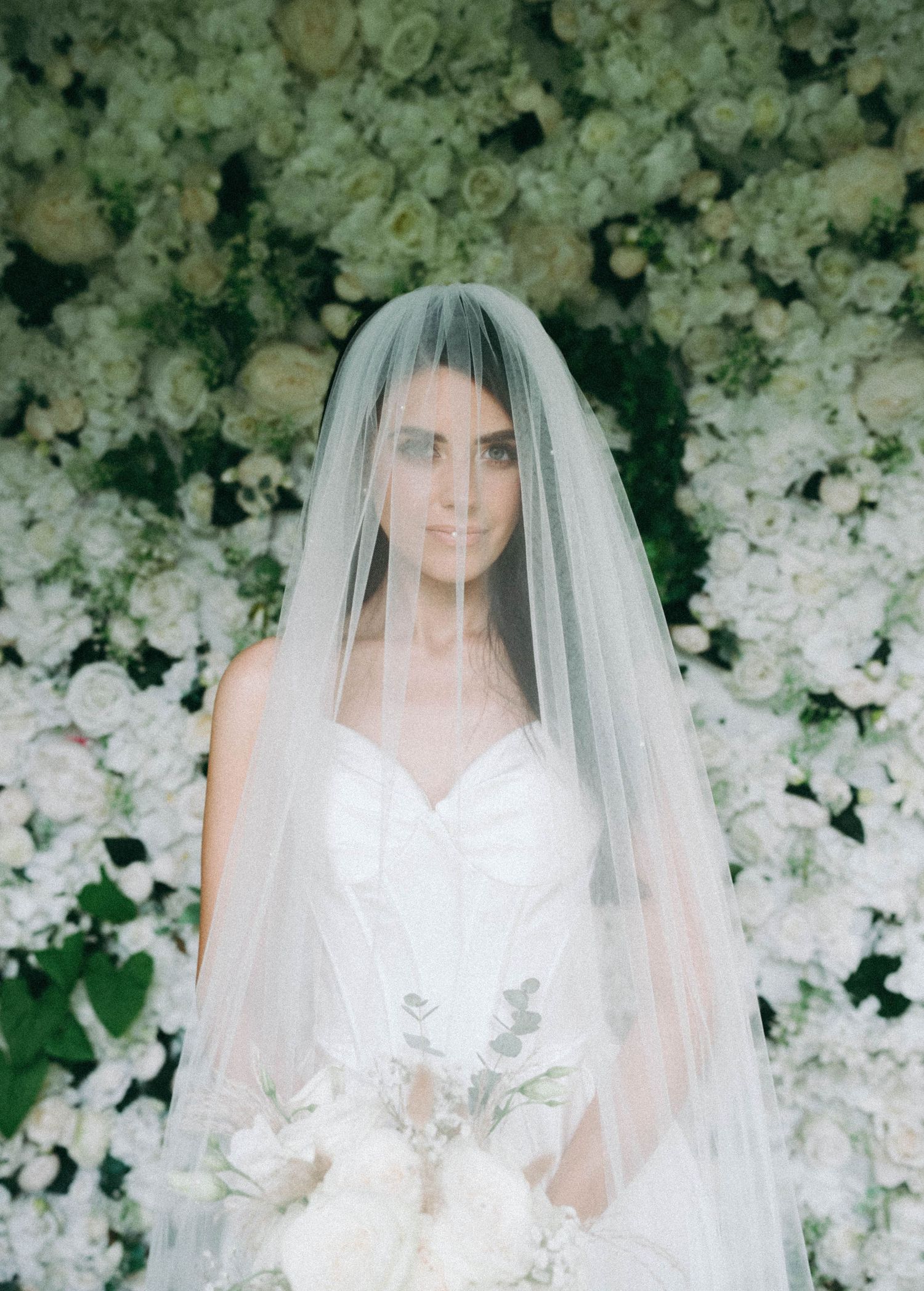 Four sequential photos show a bride in a white wedding gown and veil against a backdrop of cascading white flowers.