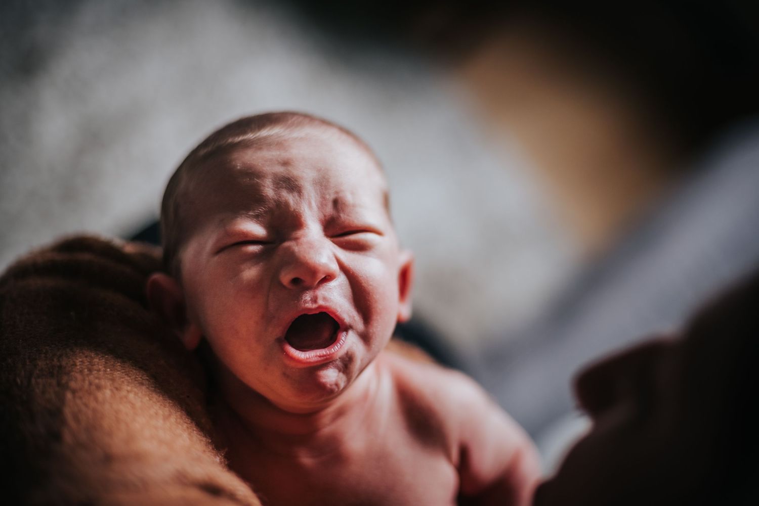 A newborn baby crying shortly after birth, shown in close-up against a dark background.