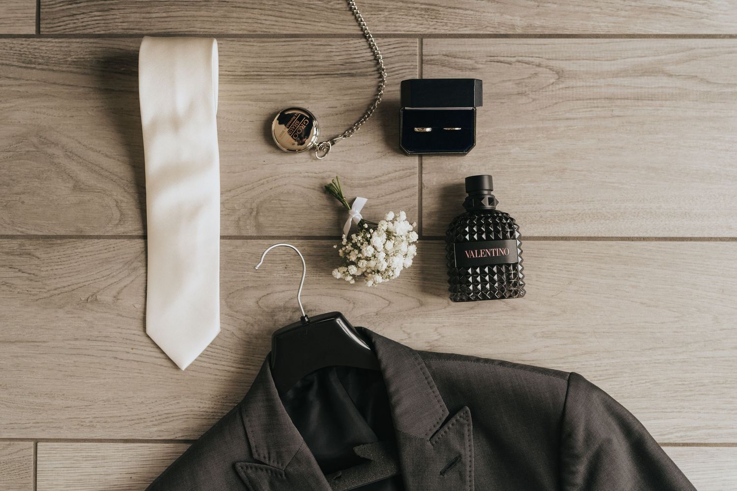 Wedding accessories including black dress shoes, a white tie and stylish cufflinks arranged on a wooden surface.