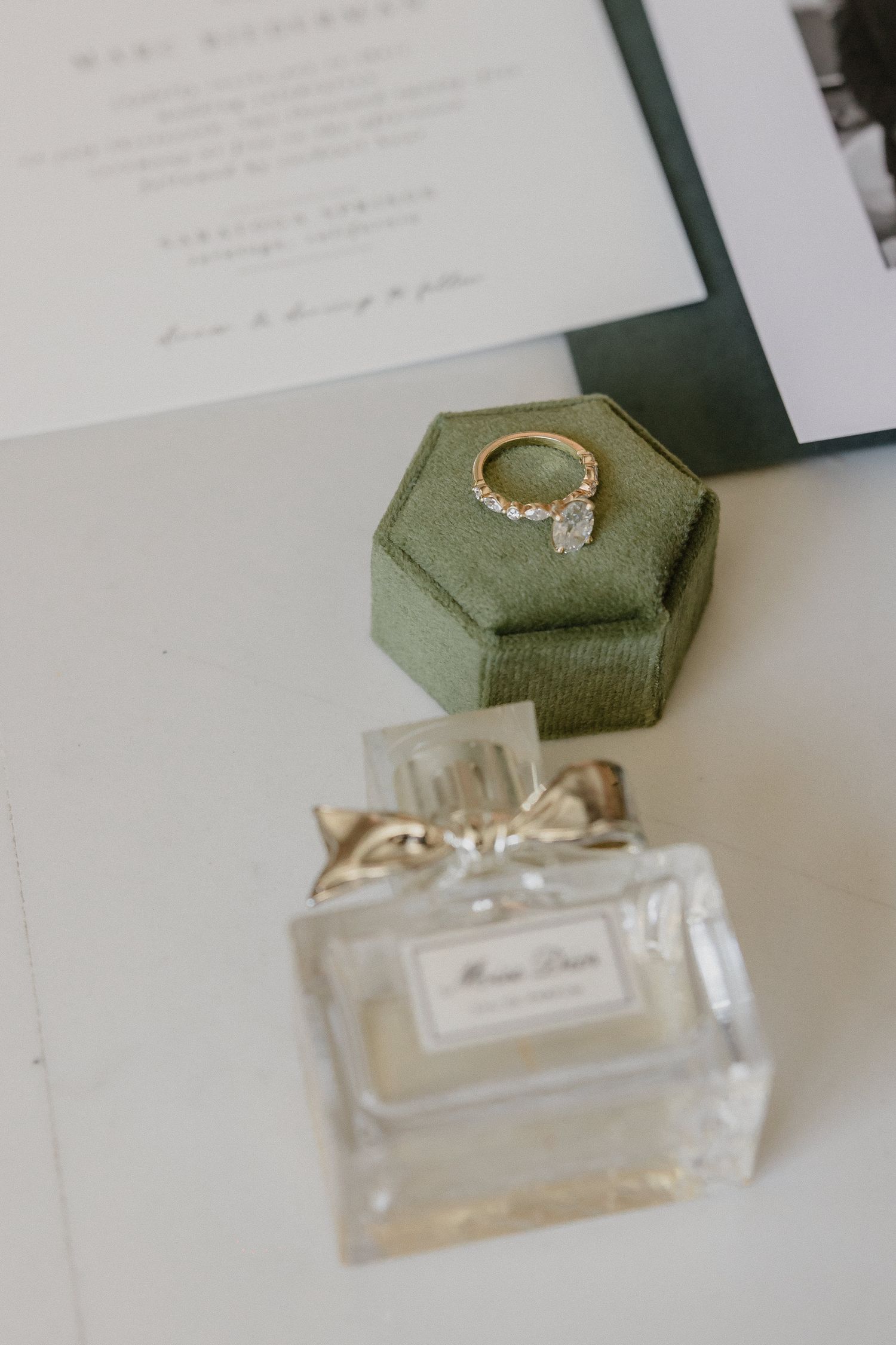Wedding details featuring perfume bottle and engagement ring on sage green velvet ring box.