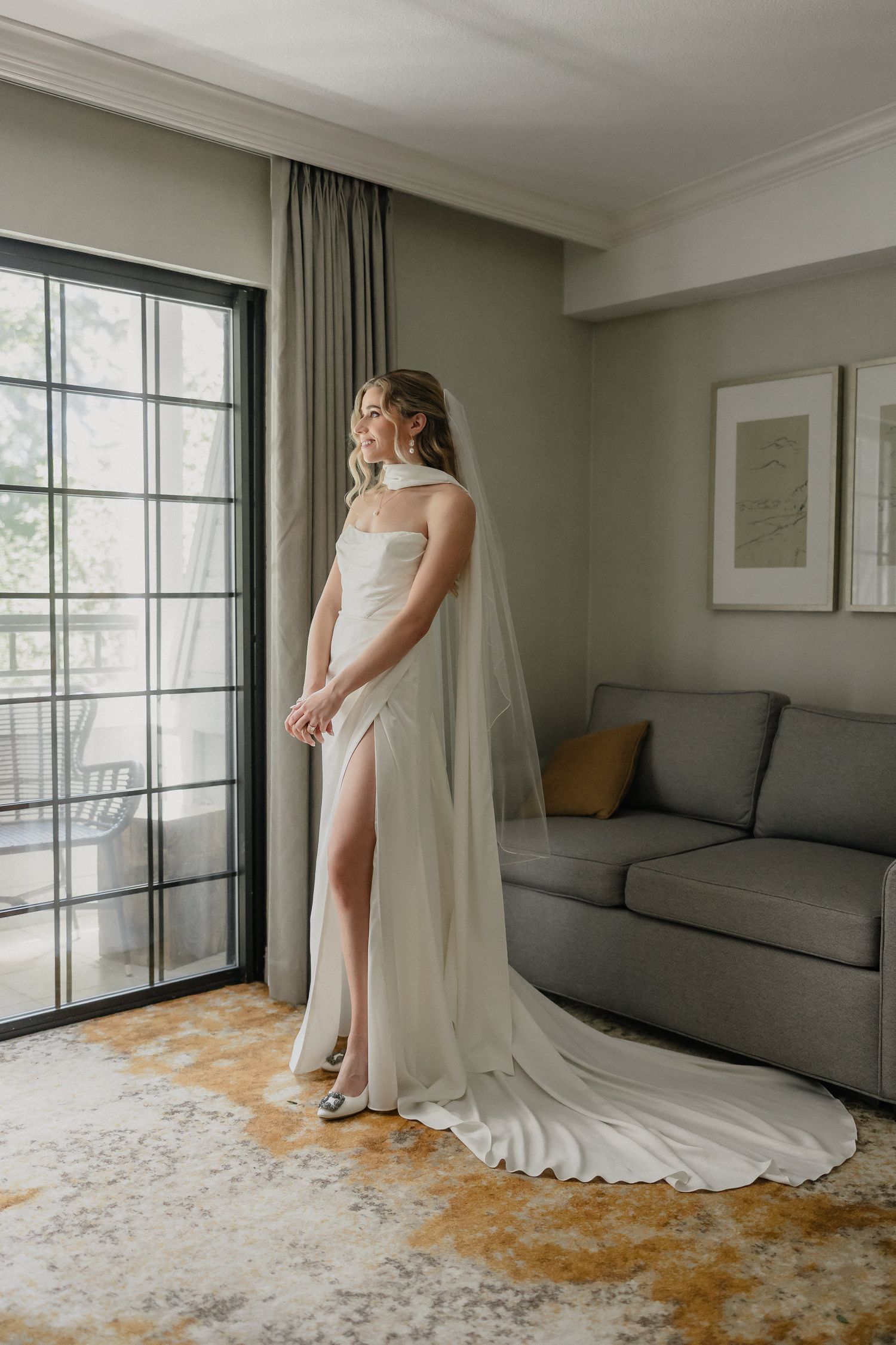 Elegant bridal preparation in a modern room with natural light and flowing white dress.