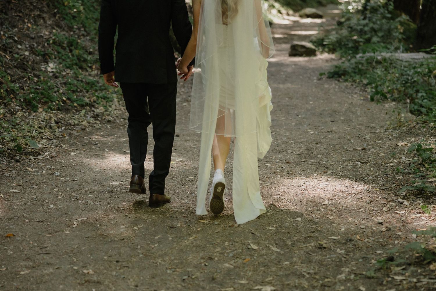 A flowing white wedding dress train trails behind on a natural pathway.
