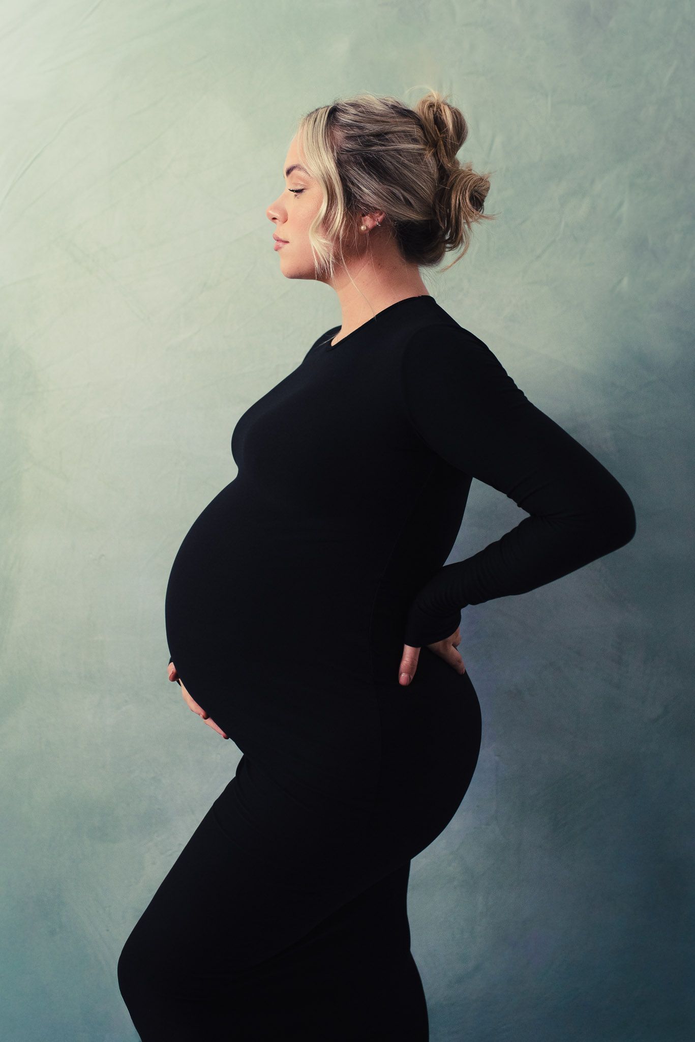 A series of four artistic maternity photos showing a woman in black against a blue-gray backdrop.