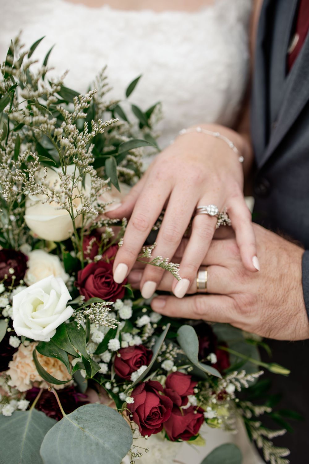 Wedding rings displayed with elegant burgundy and white floral bouquet.
