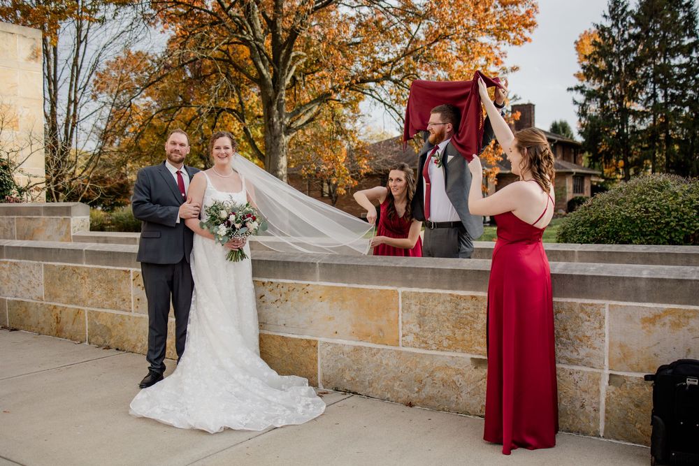 Outdoor autumn wedding ceremony with fall foliage and stone architecture in the background.
