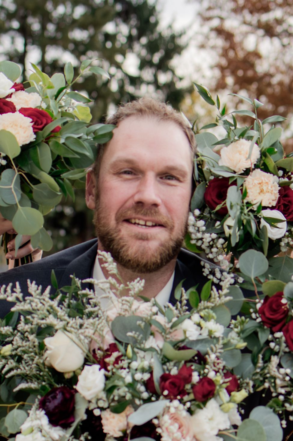 Wedding floral arrangement features burgundy and cream roses with eucalyptus greenery in an outdoor garden setting.