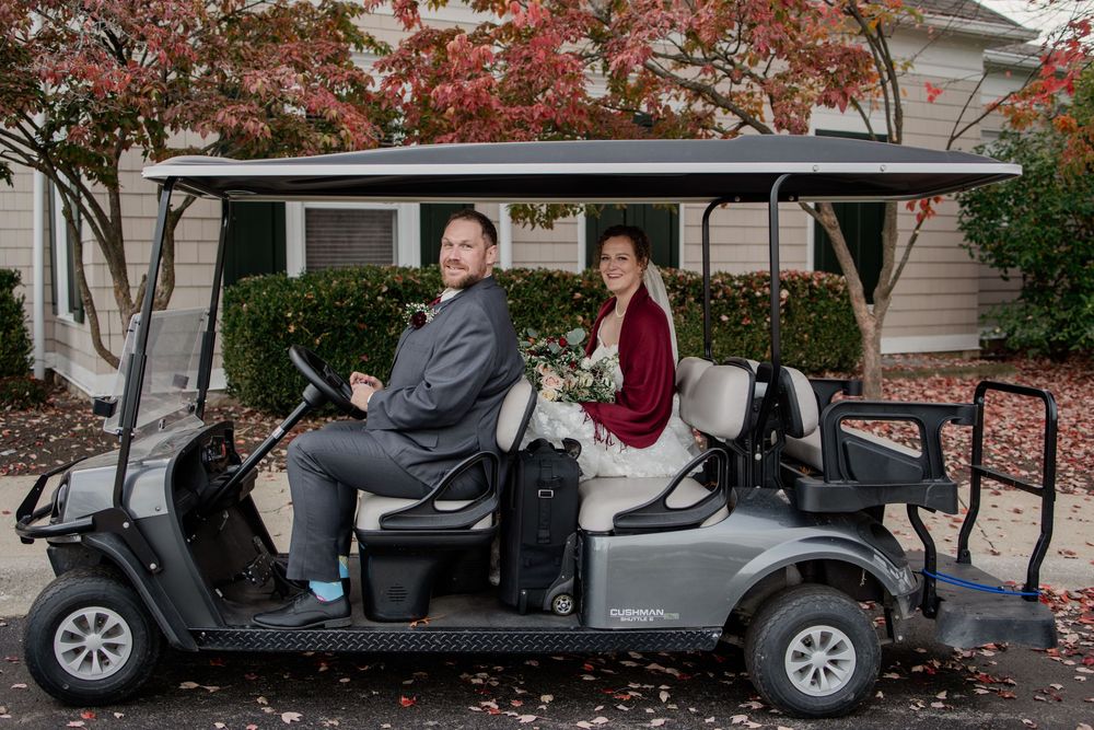 Wedding party poses with vintage car under red autumn maple trees in front of house.
