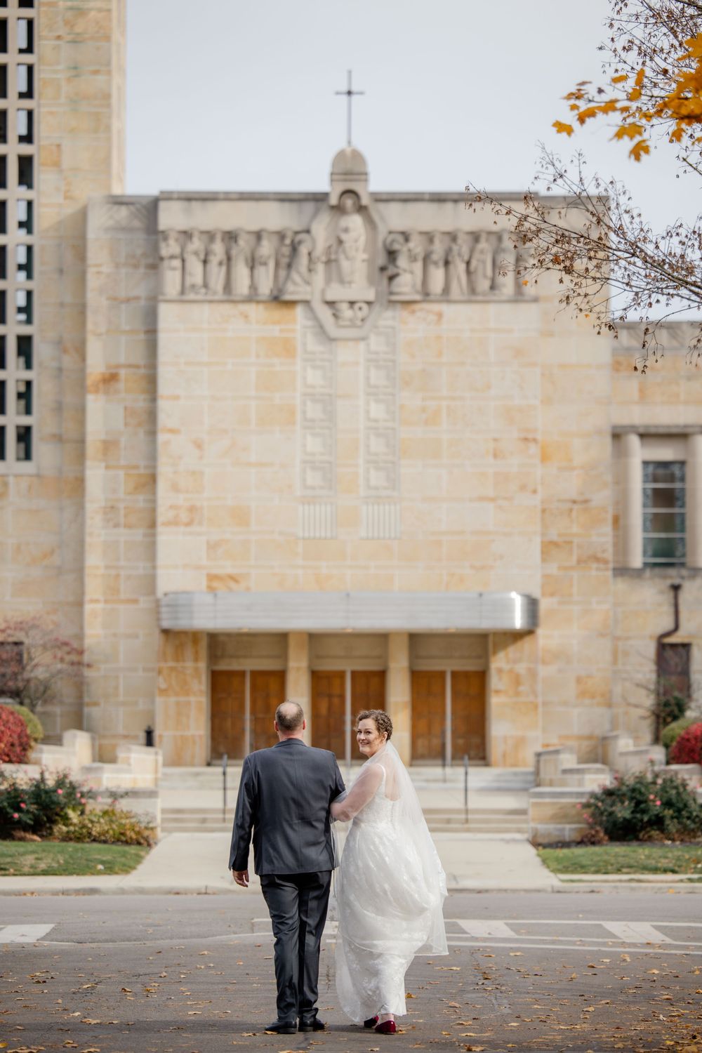 Wedding couple walking outside a grand stone church with autumn leaves falling.