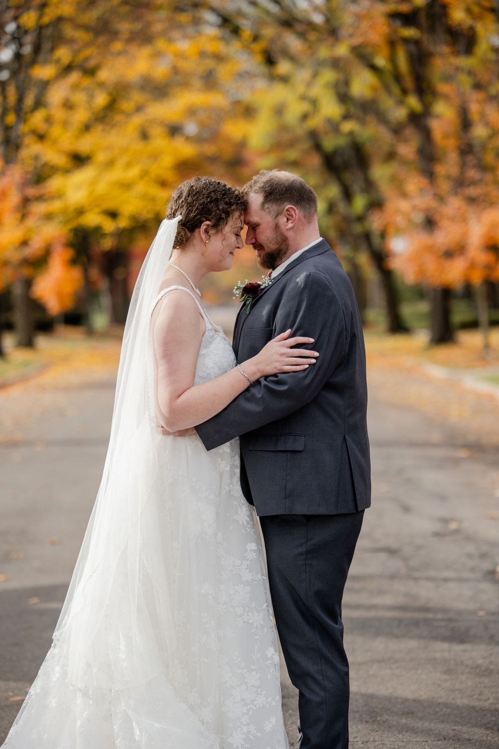A romantic wedding couple shares intimate moments in a park with golden autumn foliage in the background.