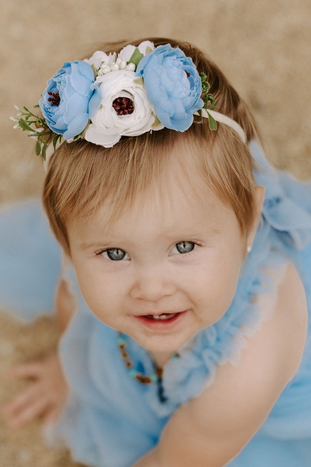 Baby wearing a delicate blue and white floral crown with a sweet smile.