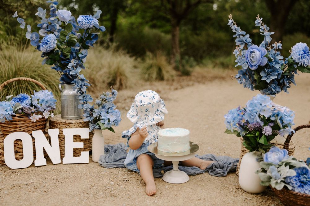 Blue hydrangea flowers and white ceramic dishes arranged on sandy ground for a rustic outdoor setting.