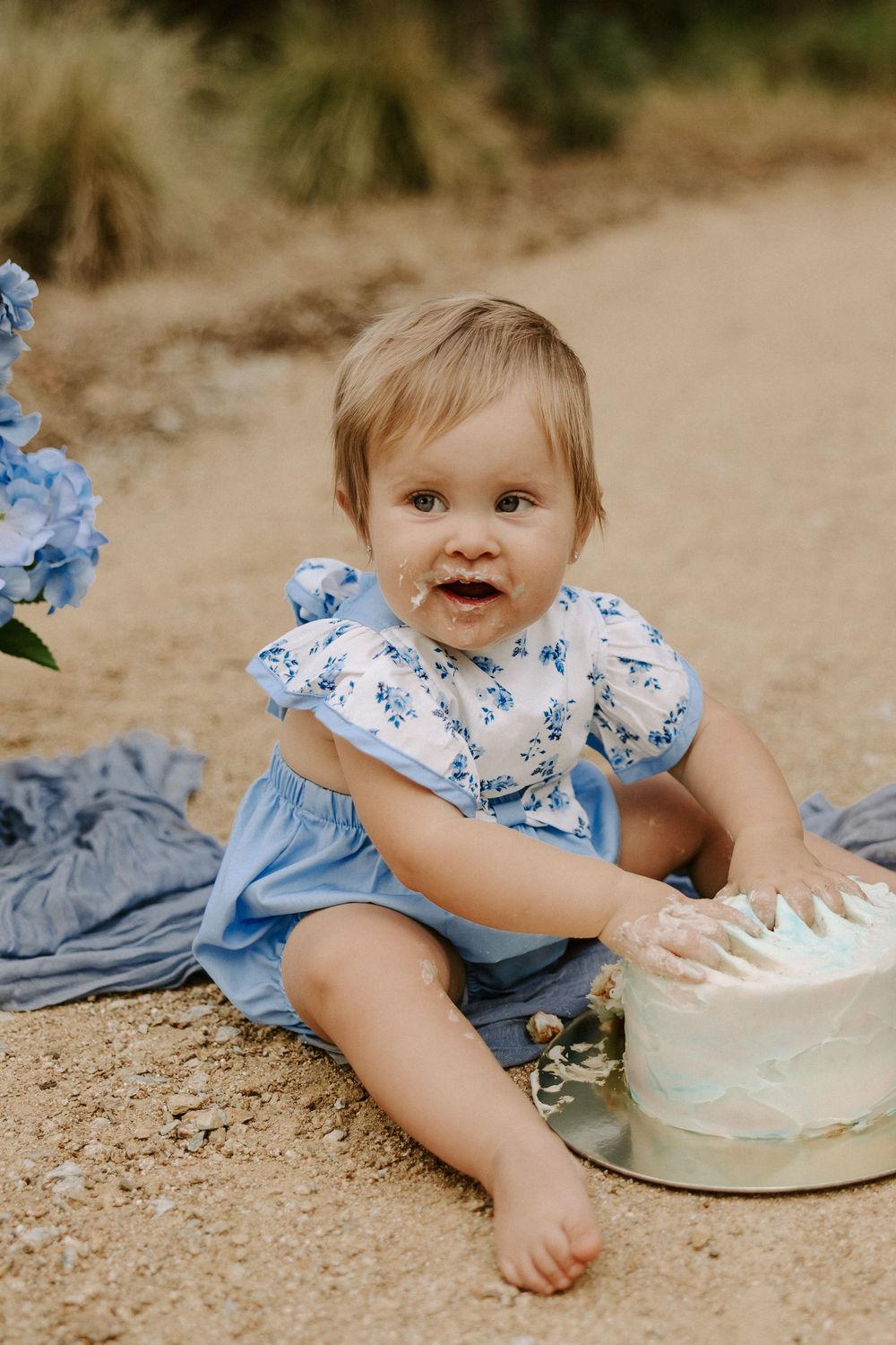 A baby in a blue and white outfit plays with a small white cake on the ground.