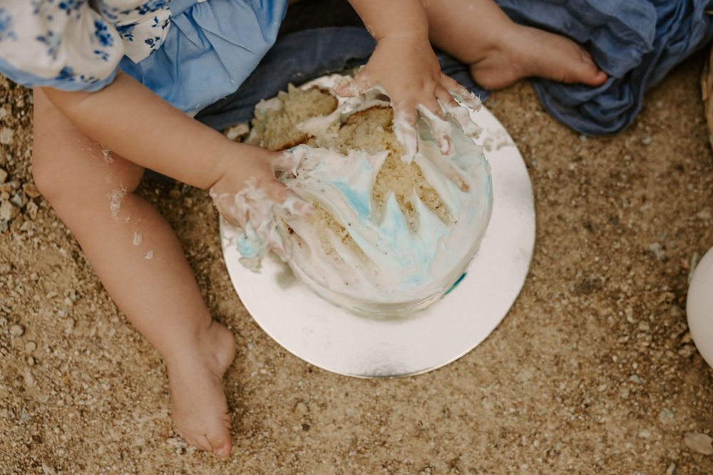 White plates with food remnants and hands reaching across a rustic wooden table surface.