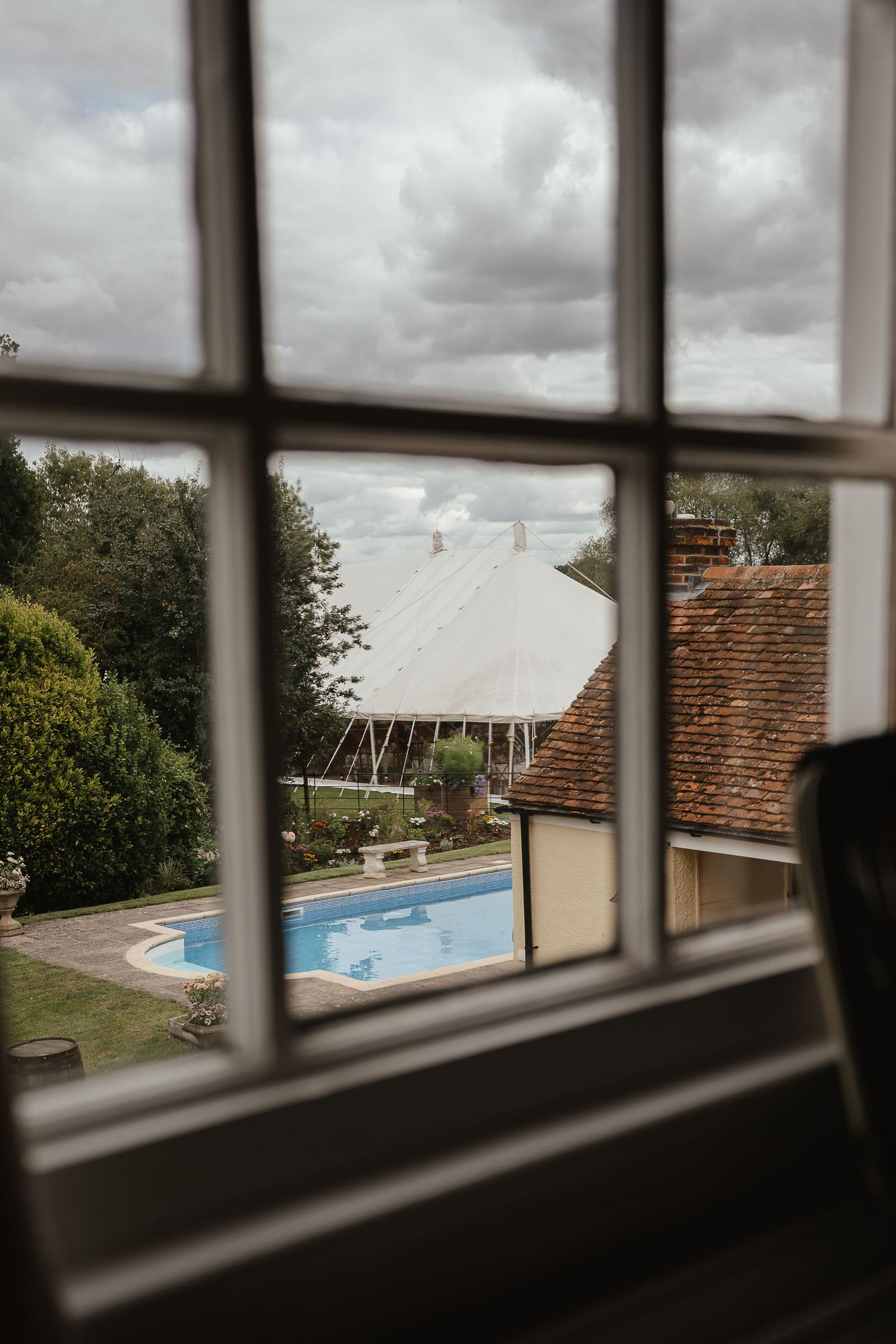 View through a window pane showing an outdoor swimming pool and cloudy sky over residential buildings.