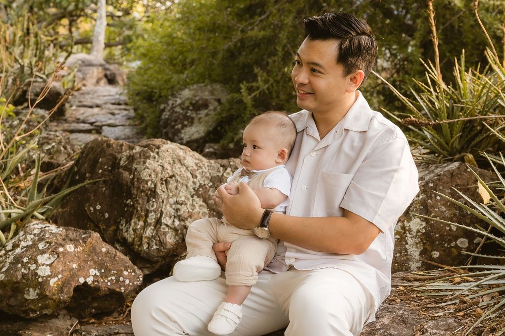 Father and baby boy sitting on rocks during a family photoshoot at Mount Coot-tha, Brisbane, captured by Joanna Kate Photography.