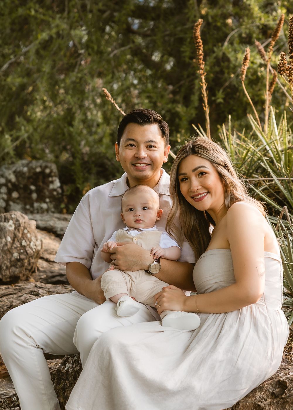 Family of three sitting on rocks surrounded by native greenery during golden hour at Mt Coot-tha Brisbane
