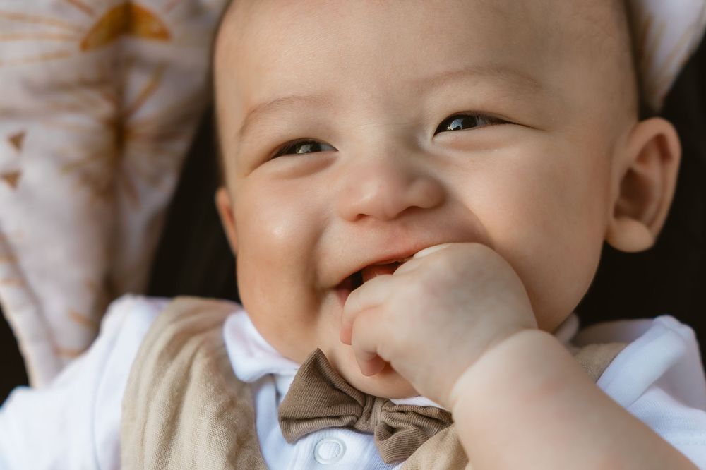 Close-up of a happy baby boy smiling with his hand in his mouth during a Brisbane family session with Joanna Kate Photography.