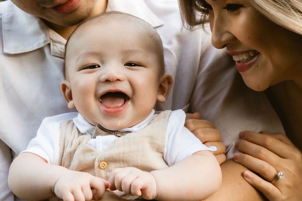 Baby boy giggling between mum and dad during a joyful family photoshoot at Mount Coot-tha in Brisbane by Joanna Kate Photography.