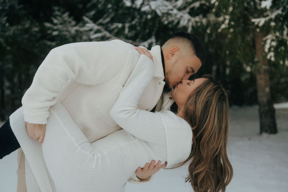 A romantic couple shares intimate moments in a snowy winter setting during an outdoor photo session.